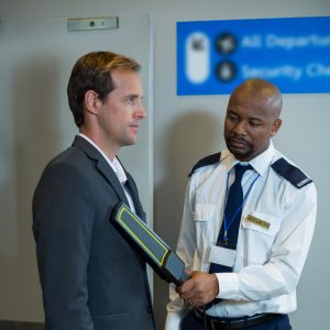 Airport security officer using a hand held metal detector to check a commuter in airport